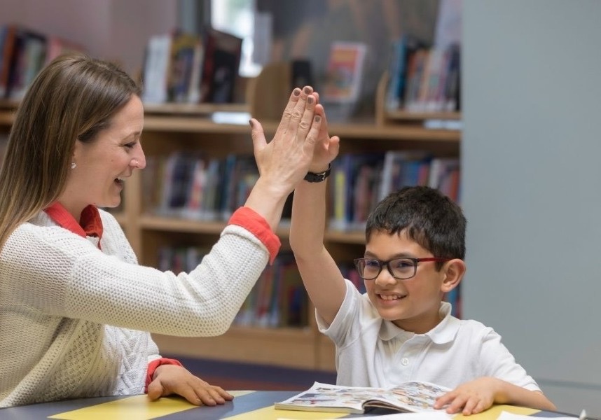 Voksen og barn gir hverandre en high five over en åpen bok